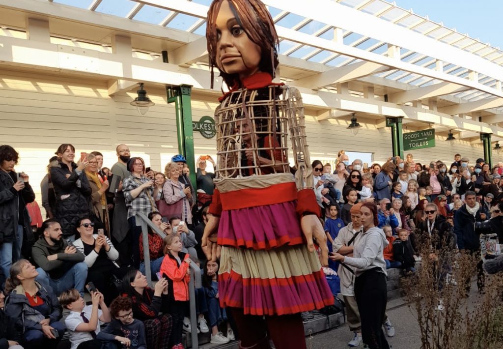 A larger than life puppet of a refugee girl is welcomed by crowds in Folkestone