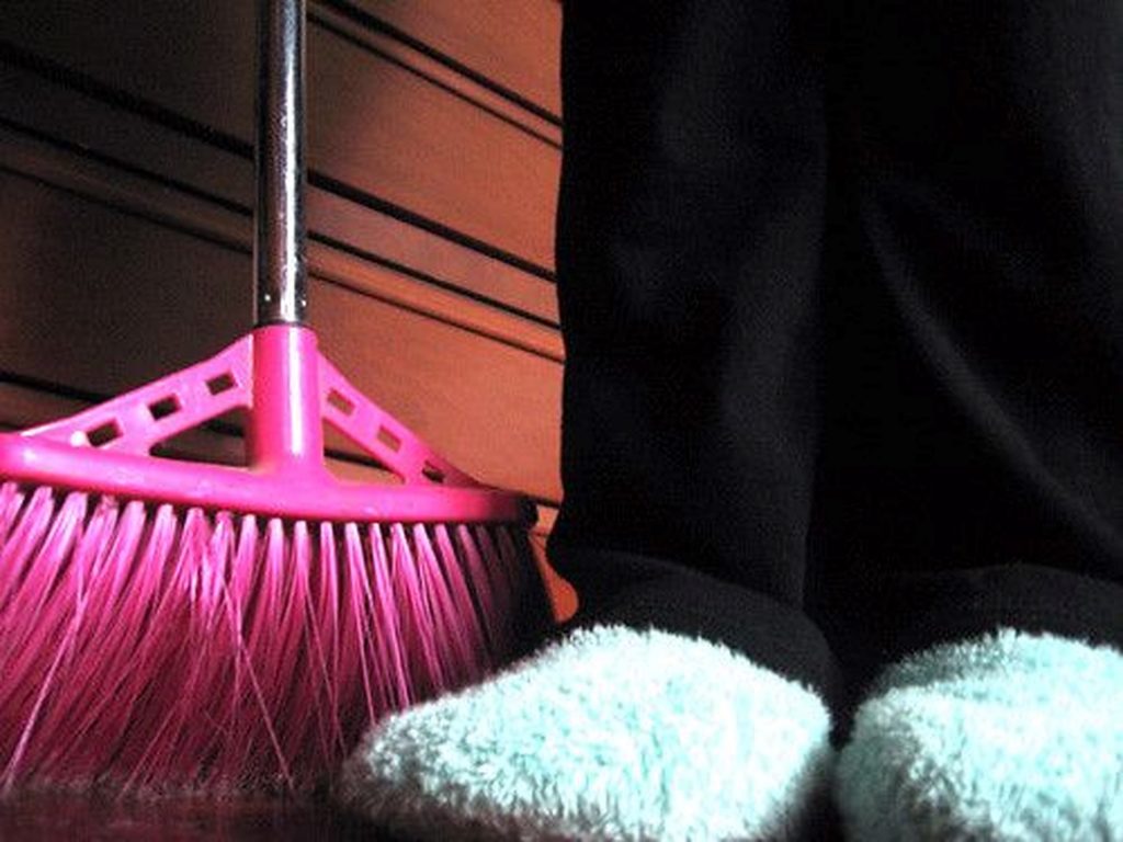 The lower legs of a person wearing fluffy slippers and holding a broom