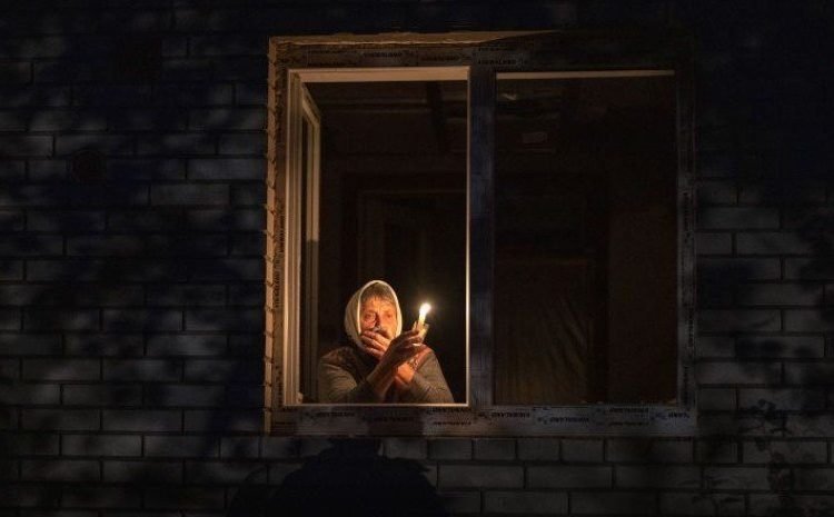 A woman holds a candle in a window in Ukraine.