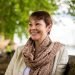 Photograph of Caroline Lucas, smiling, on a bench by the Thames