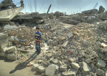 Small boy stands among the rubble of destroyed buildings in Gaza.