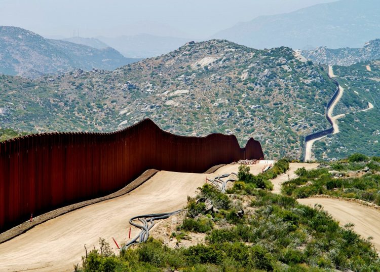 Mexican-American border: brown fencing with mountains in the background