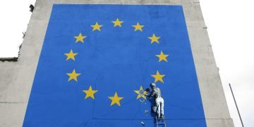 A Banksy mural showing someone chipping away at a star on the EU flag.