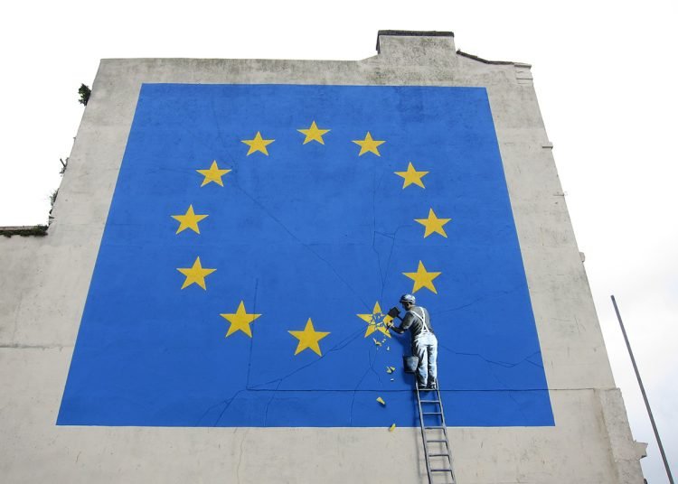 A Banksy mural showing someone chipping away at a star on the EU flag.