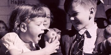 Children in a school cafeteria: girl about to bite an apple, 1950s. National Library of Medicine.