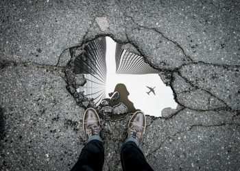 Pothole in the road with reflection of photographer showing in the puddle