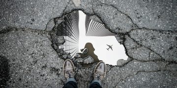 Pothole in the road with reflection of photographer showing in the puddle