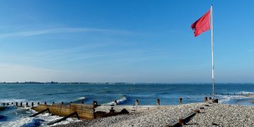 Red flag at East Head: the entrance to Chichester Harbour. Photo credit, grumpylumixuser, Wikimedia Commons