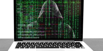 Photo of a hooded character sitting at a computer