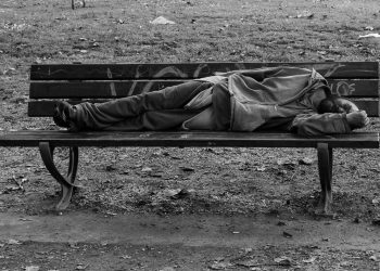 A disheveled man lying on a bench.