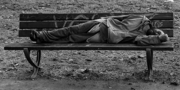 A disheveled man lying on a bench.