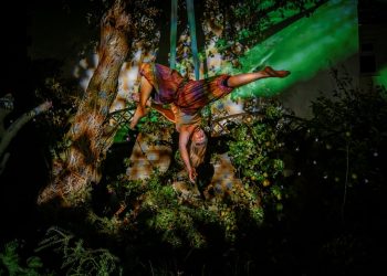A female trapeze artist suspended upside down from a rope in a woodland