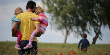 A man carrying two children across a field, while another runs off.