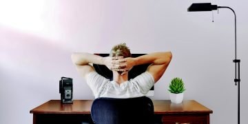 Man sitting at a desk in front of a computer with his hands behind his head