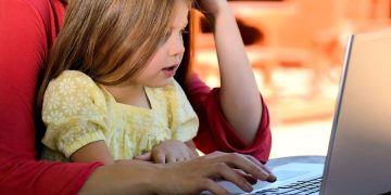 A child in a parent's arms looking at a computer