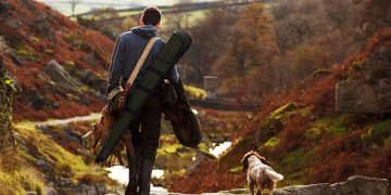 man carrying shotgun and dead birds