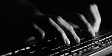 Fingers in shadow typing on a keyboard.