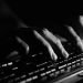 Fingers in shadow typing on a keyboard.