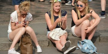 A group of girls sitting outside whilst scrolling on their phones.