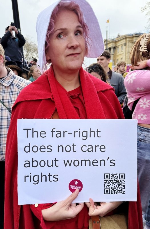 Woman dressed in The Handmaid's Tale costume carrying a banner that reads "The far-right does not care about women's rights"
