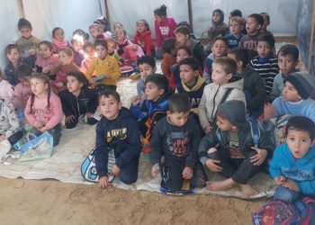 A group of children sit ready to learn in a tent acting as a makeshift school.