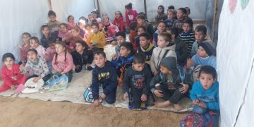 A group of children sit ready to learn in a tent acting as a makeshift school.