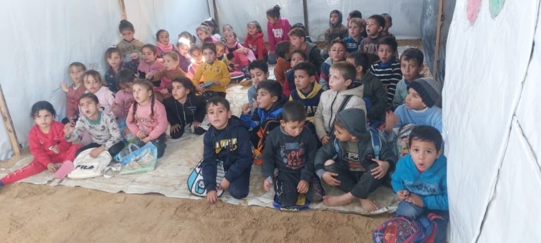 A group of children sit ready to learn in a tent acting as a makeshift school.