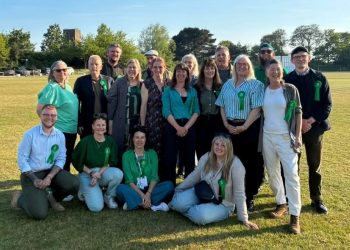 Group of adults posing on a sunny grassy field, all wearing green ribbons, suggesting a charity or awareness event.