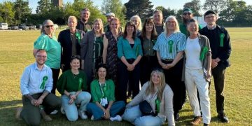Group of adults posing on a sunny grassy field, all wearing green ribbons, suggesting a charity or awareness event.