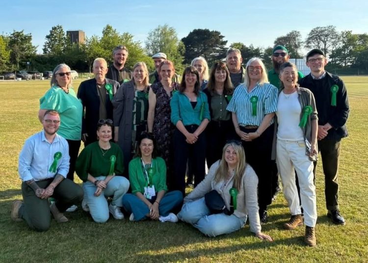 Group of adults posing on a sunny grassy field, all wearing green ribbons, suggesting a charity or awareness event.