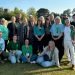 Group of adults posing on a sunny grassy field, all wearing green ribbons, suggesting a charity or awareness event.