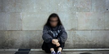 Person sitting on the ground in front of a wall