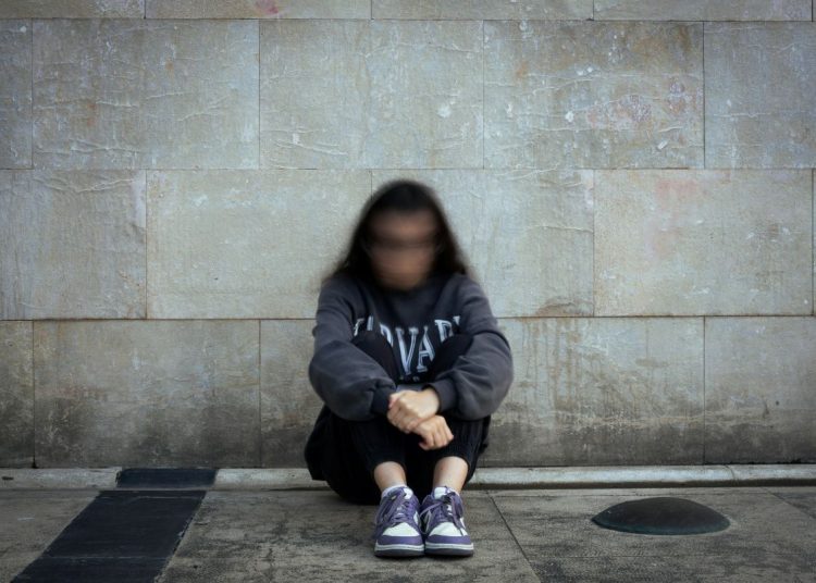 Person sitting on the ground in front of a wall