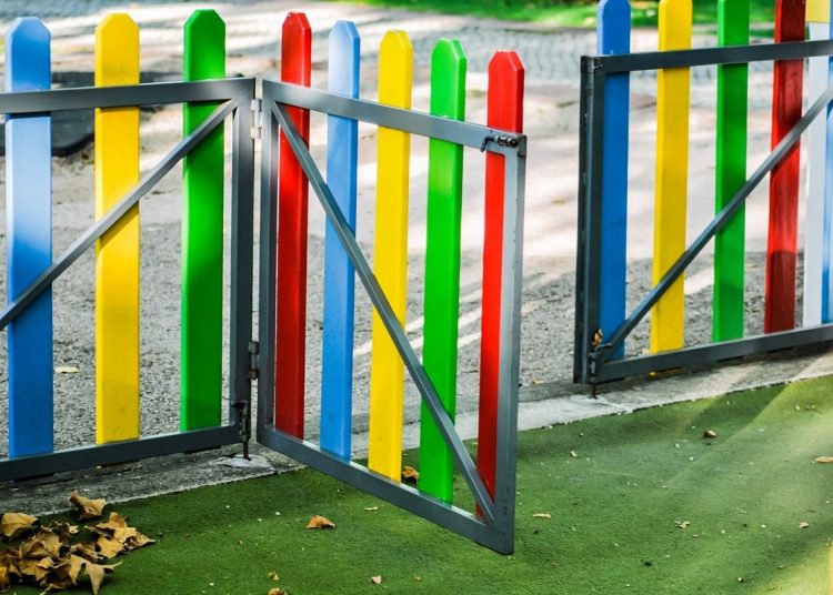 Colorful playground fence gate with blue, yellow, green, and red slats and a gray metal frame.
