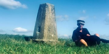 man sits by a trig point on Heyshott Down