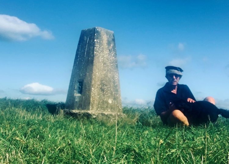 man sits by a trig point on Heyshott Down